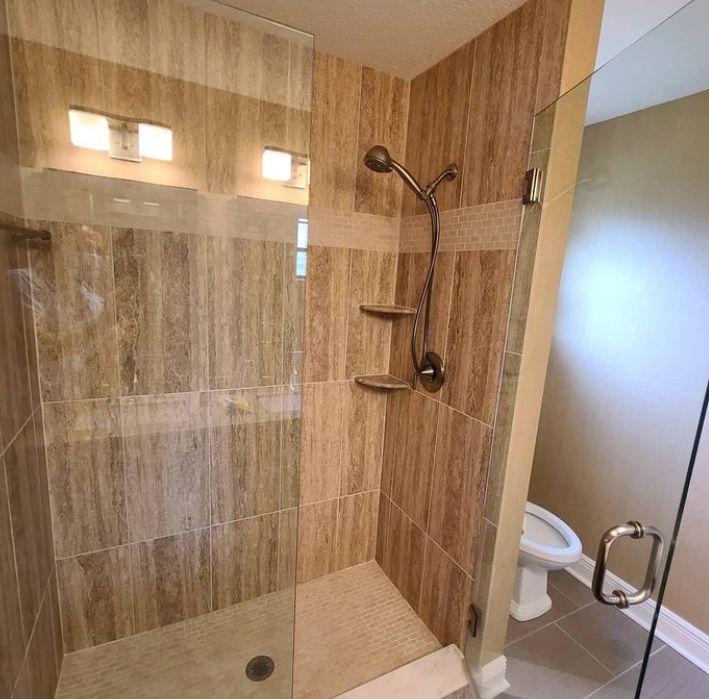 Modern tiled shower with a glass door, wall-mounted showerhead, and built-in shelves.