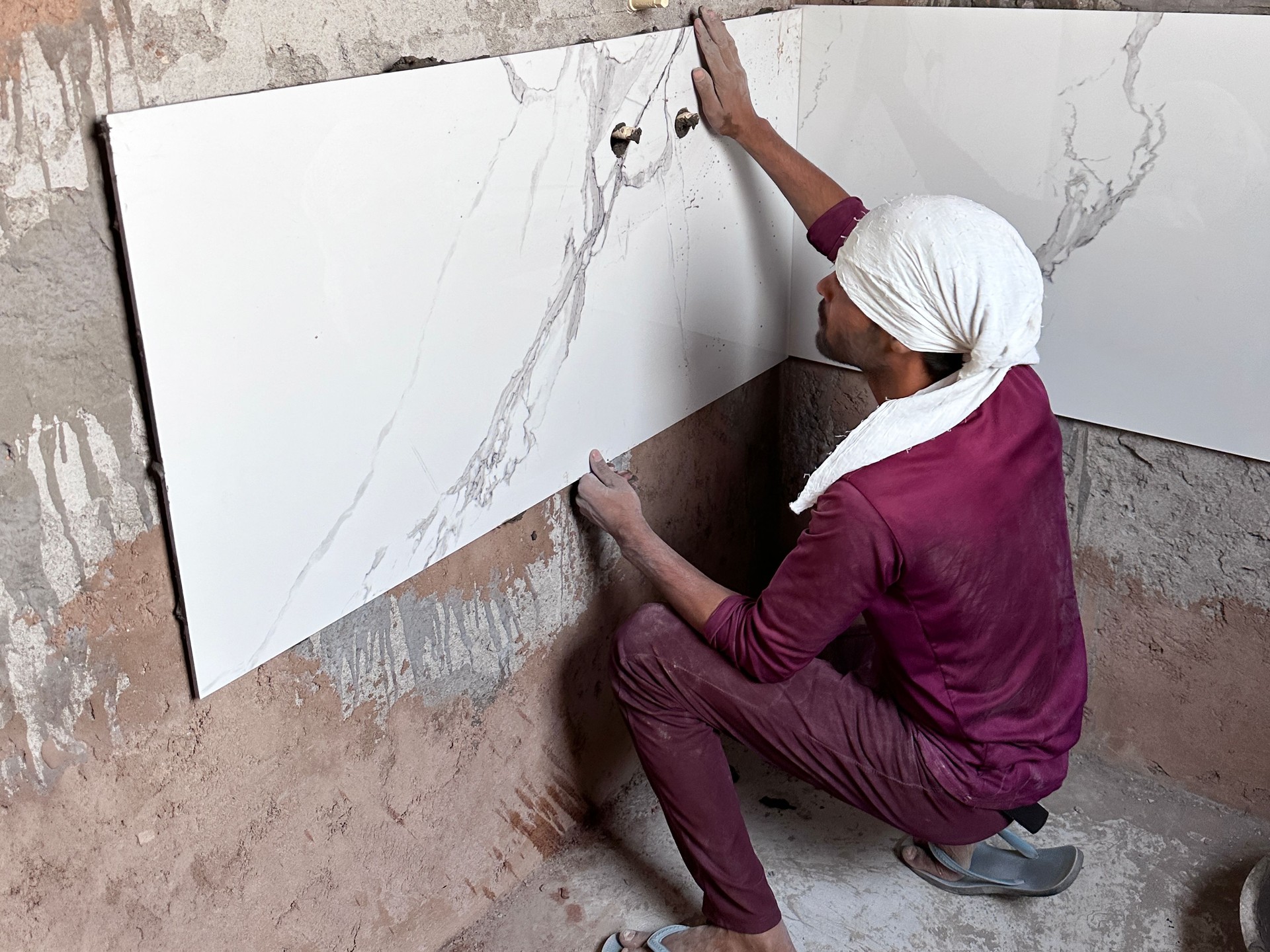 Image of professional tiler installing large white and grey marble tiles in bathroom, rectangular brick pattern / home improvement and renovation project